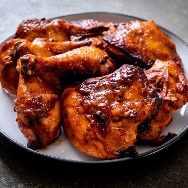 A white plate filled with glistening, golden-brown grilled chicken pieces, including drumsticks and thighs.