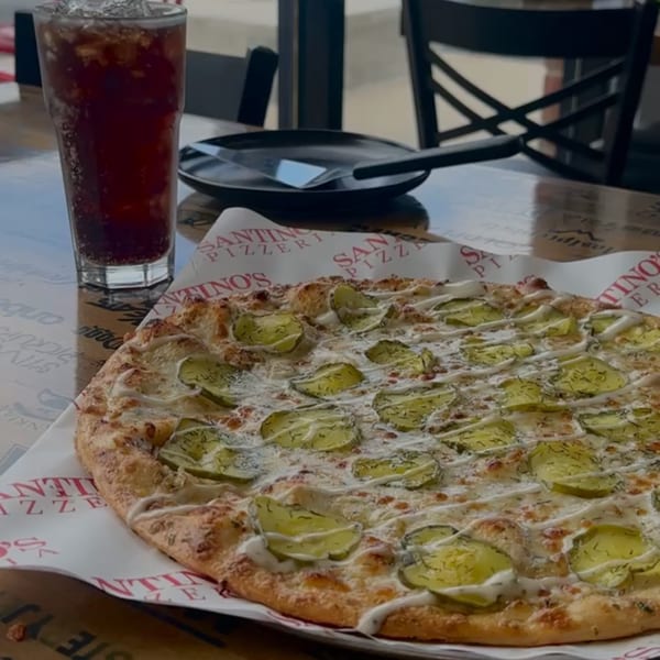 A Santino's Pizzeria pickle pizza with white sauce and dill, next to a glass of soda.
