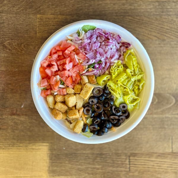 A Santino's Pizzeria salad with tomatoes, red onions, croutons, black olives, and banana peppers.