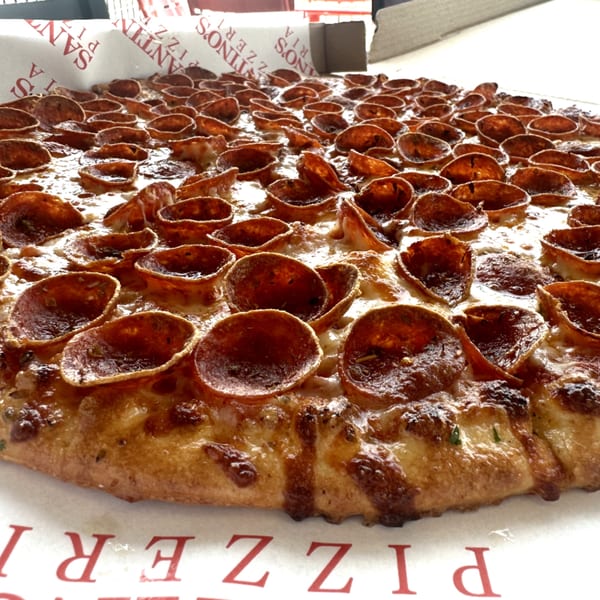 A close-up of a Santino's Pizzeria pepperoni pizza with crispy, curled pepperoni in a box.