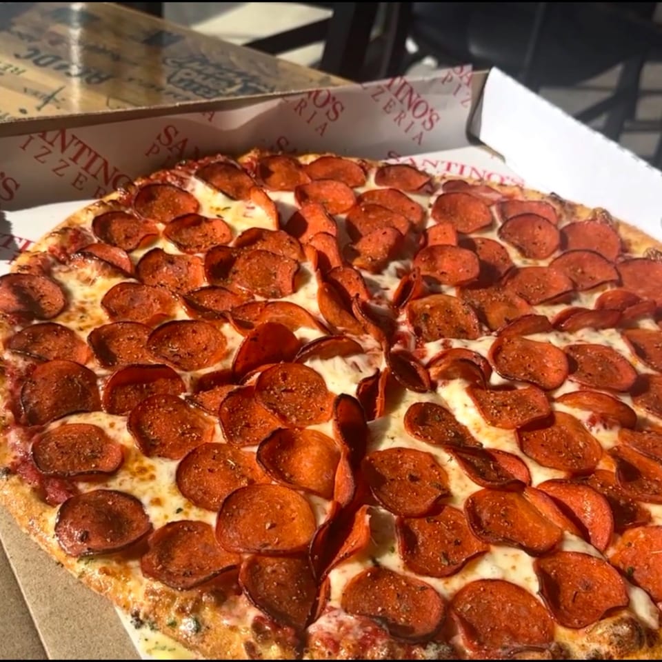 A close-up of a Santino's Pizzeria pepperoni pizza in a box, with melted cheese and crispy pepperoni.