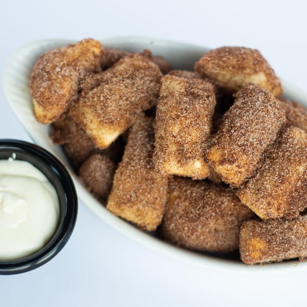 A white bowl filled with cinnamon sugar dessert bites and a side of white dipping sauce.